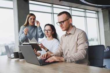 Büyük pencereli bir ofiste çalışmak, meslektaşlar taşınabilir bir dizüstü bilgisayar kullanarak yeni bir proje üzerinde çalışıyorlar. Çalışanlarla modern ofis.