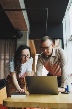 Tatmin olmuş genç bir adam bayan bir meslektaşıyla konuşur ve yapılan işten memnun kalır. Meslektaşlar ofiste dizüstü bilgisayarda çalışır. Modern bir ofis alanında çalışmak.