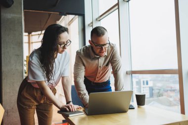 Tatmin olmuş genç bir adam bayan bir meslektaşıyla konuşur ve yapılan işten memnun kalır. Meslektaşlar ofiste dizüstü bilgisayarda çalışır. Modern bir ofis alanında çalışmak.