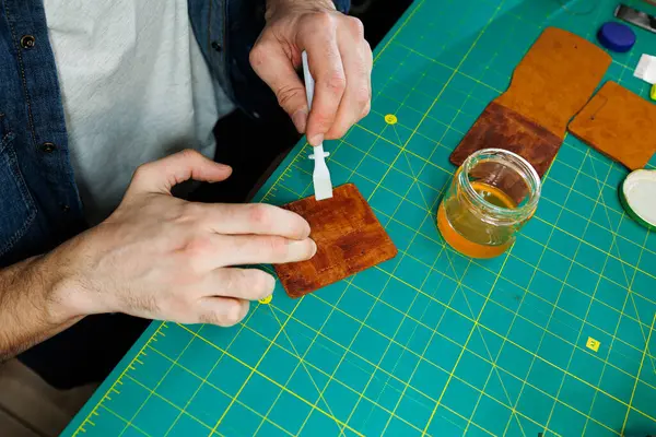 ご主人様の手縫いの革製品 男性の手は 品質の革アクセサリーを作成し 部品を接続します 革工房での作業工程 ロイヤリティフリーのストック写真