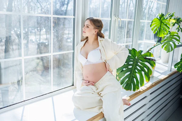 Beyaz Takım Elbiseli Şık Hamile Bir Kadın Pencere Eşiğinde Oturuyor — Stok fotoğraf