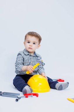 Küçük bir çocuk beyaz bir arka planda bir oyuncak set inşaatçı aletleriyle oynuyor. Çocuk plastik oyuncakları..
