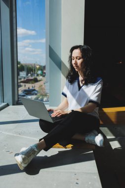 İş sırasında dizüstü bilgisayarında yaratıcı fikirler arayan başarılı bir kadın. Modern çalışma alanında otururken internet üzerinden iş haberleri okuyan pozitif kız öğrenci