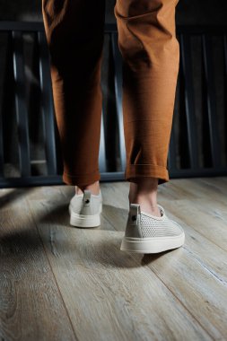 Beyaz deri ayakkabılarla kadın bacaklarının yakın çekimi. Yazlık kadın ayakkabıları koleksiyonu. Bağcıklı beyaz kadın ayakkabıları.