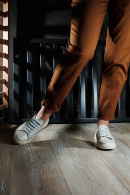 Deri ayakkabılı kadın bacaklarının yakın çekimi. Deri şık beyaz ayakkabılar içinde kahverengi pantolonlu genç bir kadın. Yaz kadın ayakkabıları. Sıradan sokak tarzı.