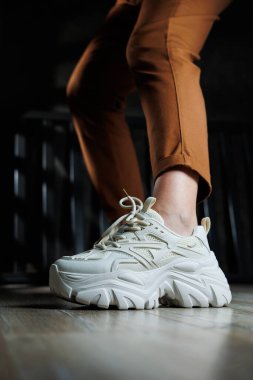 Yüksek tabanlı beyaz deri ayakkabılarla kadın bacaklarının yakın çekimi. Yazlık kadın ayakkabıları koleksiyonu. Bağcıklı beyaz kadın ayakkabıları.