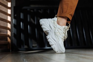 Beyaz spor ayakkabılarla kadın bacaklarına yakın çekim. Bağcıklı kadın yaz ayakkabıları..