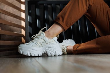 Beyaz spor ayakkabılarla kadın bacaklarına yakın çekim. Bağcıklı kadın yaz ayakkabıları..