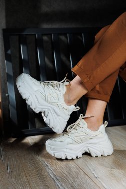 Kadınlar için yazlık deri spor ayakkabıları koleksiyonu. Beyaz spor ayakkabılarla kadın bacaklarına yakın çekim. Bağcıklı kadın yaz ayakkabıları..
