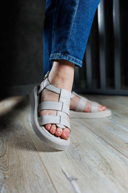 Gri parke üzerinde deri sandaletli güzel, narin kadın bacakları. Kadın sandaleti koleksiyonu