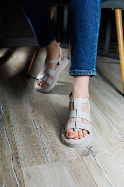 Gri parke üzerinde deri sandaletli güzel, narin kadın bacakları. Kadın sandaleti koleksiyonu