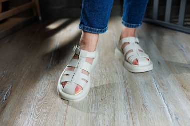 İnce kadın bacakları, topuksuz bej deri sandaletler içinde. Kadınların yaz sandaletleri koleksiyonu.