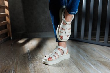 İnce kadın bacakları, topuksuz bej deri sandaletler içinde. Kadınların yaz sandaletleri koleksiyonu.