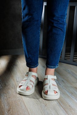 İnce kadın bacakları, topuksuz bej deri sandaletler içinde. Kadınların yaz sandaletleri koleksiyonu.