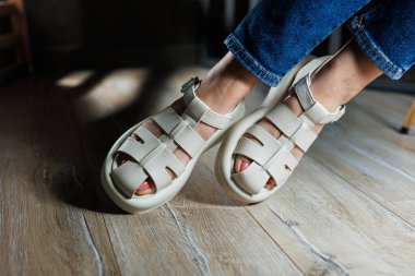 İnce kadın bacakları, topuksuz bej deri sandaletler içinde. Kadınların yaz sandaletleri koleksiyonu.