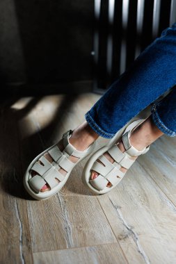 İnce kadın bacakları, topuksuz bej deri sandaletler içinde. Kadınların yaz sandaletleri koleksiyonu.