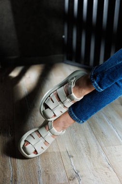 İnce kadın bacakları, topuksuz bej deri sandaletler içinde. Kadınların yaz sandaletleri koleksiyonu.