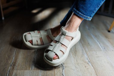 İnce kadın bacakları, topuksuz bej deri sandaletler içinde. Kadınların yaz sandaletleri koleksiyonu.