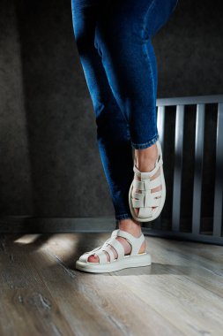 Kadın deri sandaletlerinin koleksiyonu. İnce kadın bacakları, topuksuz bej deri sandaletler içinde..