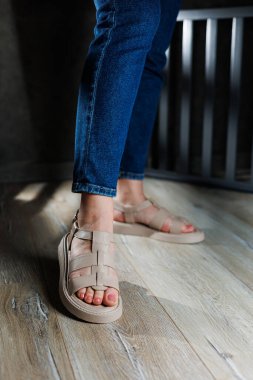 Kadın deri sandaletlerinin koleksiyonu. İnce kadın bacakları, topuksuz bej deri sandaletler içinde..