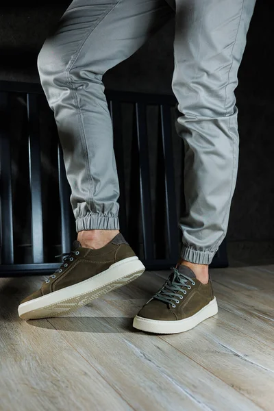 Close-up of male feet in green leather shoes. A young man is standing in leather stylish green sneakers in gray jeans. Summer men's shoes. Casual street style