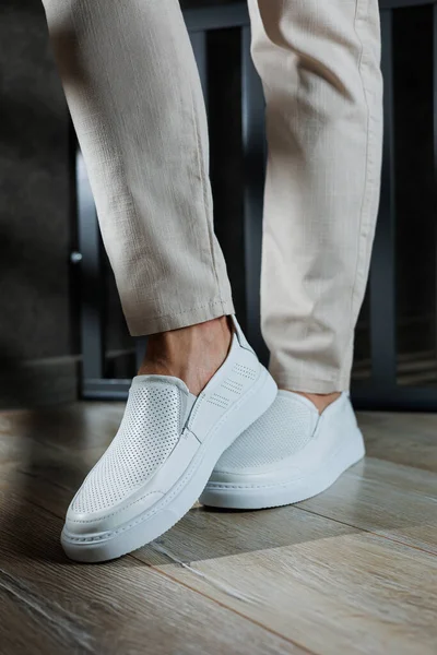 Close-up of male feet in white casual shoes. Fashionable young man standing in leather stylish white moccasins in fashionable trousers. Seasonal summer men\'s shoes. Casual street style.