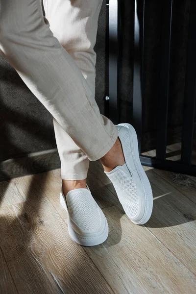 Close-up of male feet in white casual shoes. Fashionable young man standing in leather stylish white moccasins in fashionable trousers. Seasonal summer men\'s shoes. Casual street style.