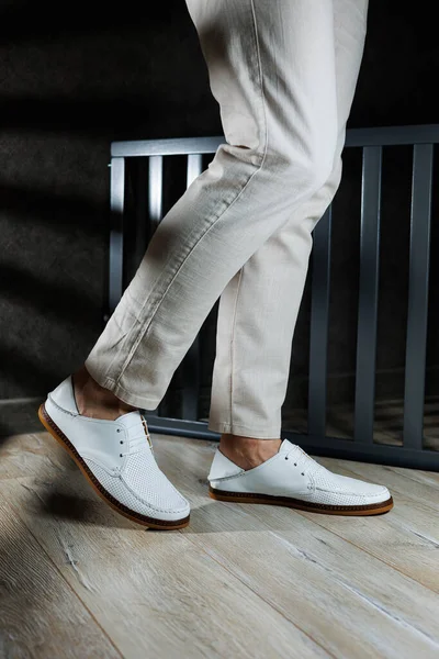 Male feet close-up in white casual shoes. Fashionable young man standing in leather stylish white moccasins in trousers. Seasonal summer men\'s shoes. Casual street style.