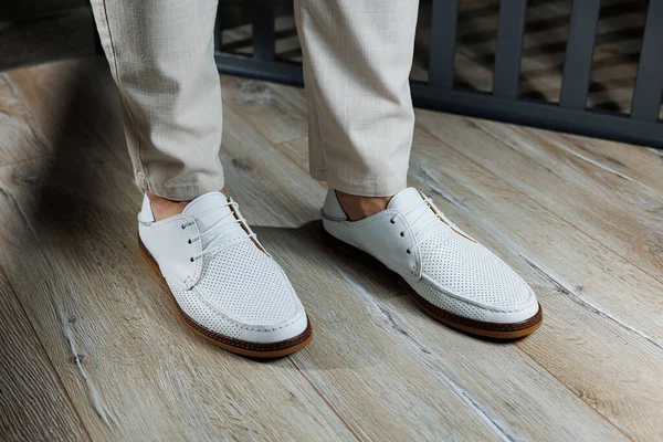 Male feet close-up in white casual shoes. Fashionable young man standing in leather stylish white moccasins in trousers. Seasonal summer men\'s shoes. Casual street style.