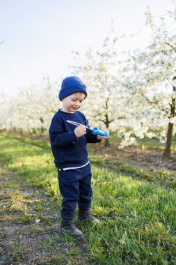 Üç yaşında bir çocuk çiçek açan bir bahçede sabun köpüğüyle koşuyor. Neşeli, duygusal çocuk parkta yürüyor. Çocuklar için sabun çubukları