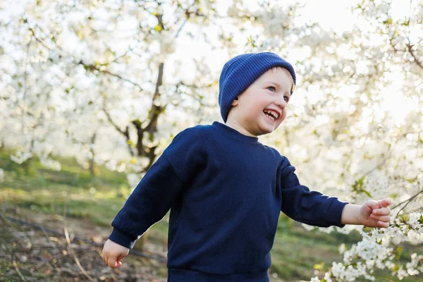 stock image A three-year-old boy runs through a blooming garden. Cheerful emotional child is walking in the park.