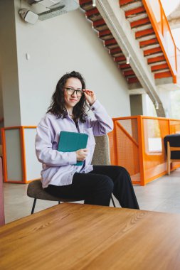 Başarılı bir kadın, günlük giysiler içinde gözlük takıyor modern kafedeki rahat koltukta oturuyor ve tablet internette çalışıyor. Uzaktan kumanda. Bağımsız bir çalışanın işi