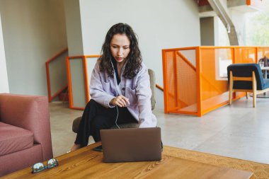 Modern bir kafede, dizüstü bilgisayarlı bir masada oturan gözlüklü genç bir kadın. Kulaklıkla konuşan bir kadın var. Uzaktan kumanda. Bağımsız bir çalışanın işi