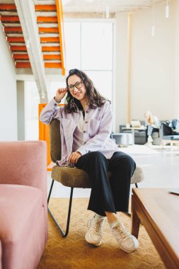 Gözlüklü şık bir kadın modern bir kafede oturmuş internetteki telefonuyla çalışıyor. Kulaklıkla konuşan bir kadın var. Uzaktan kumanda. Bağımsız bir çalışanın işi