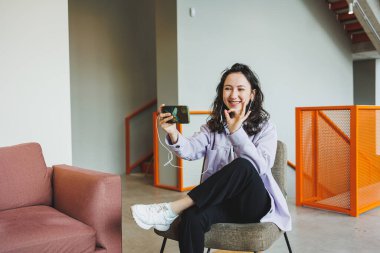 Gözlüklü şık bir kadın modern bir kafede oturmuş internetteki telefonuyla çalışıyor. Kulaklıkla konuşan bir kadın var. Uzaktan kumanda. Bağımsız bir çalışanın işi