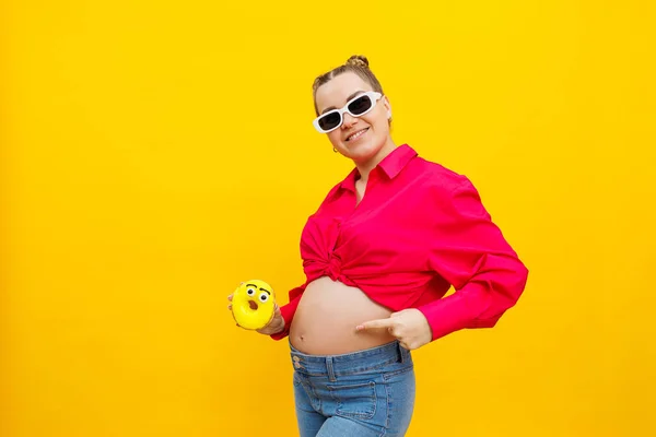 黄色の背景に甘い黄色のドーナツを手にした陽気妊娠中の女性 母親を期待しています 健康的で不健康な食品 食事療法の概念 ジャンクフード — ストック写真