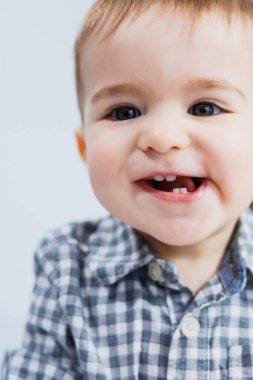 Bir yaşında, beyaz arka planda, kareli gömlekli küçük bir çocuk. Yüzünde gülümseme olan küçük bir çocuk..