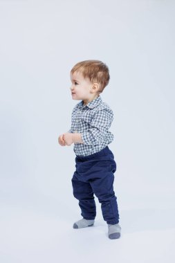 Bir yaşında, beyaz arka planda, kareli gömlekli küçük bir çocuk. Yüzünde gülümseme olan küçük bir çocuk..