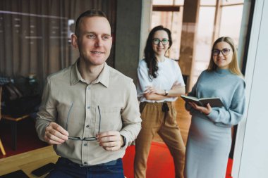 Ofiste arka planda bir grup meslektaşla birlikte dizüstü bilgisayar üzerinde çalışan kendine güvenen genç iş adamları. Modern bir ofisteki meslektaşların işi..