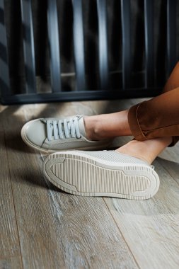 Bej renkli spor ayakkabılarla dar pantolonlu, ince kadın bacakları. Kadın deri ayakkabıları..