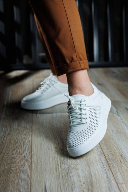 Pantolonlu ince kadın bacakları, beyaz spor ayakkabılarıyla yakın plan. Kadın deri ayakkabıları..