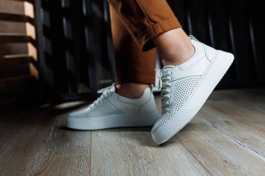 Pantolonlu ince kadın bacakları, beyaz spor ayakkabılarıyla yakın plan. Kadın deri ayakkabıları..