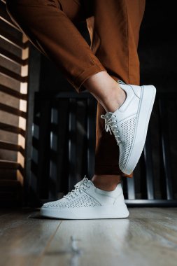Pantolonlu ince kadın bacakları, beyaz spor ayakkabılarıyla yakın plan. Kadın deri ayakkabıları..