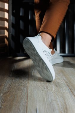 Pantolonlu ince kadın bacakları, beyaz spor ayakkabılarıyla yakın plan. Kadın deri ayakkabıları..