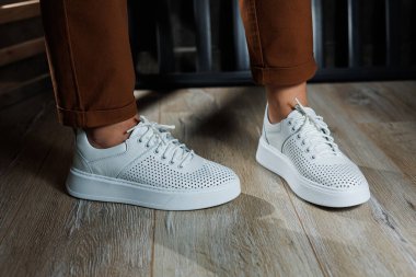 Pantolonlu ince kadın bacakları, beyaz spor ayakkabılarıyla yakın plan. Kadın deri ayakkabıları..