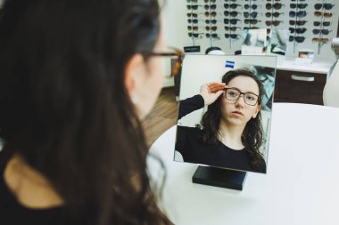 Optik dükkanı. Genç bir kadın bir optik mağazada gözlük seçer. Gözlüklü dur. Vizyon düzeltmesi. Gözlüklü kadın. Gözlüklü bir kadının portresi..