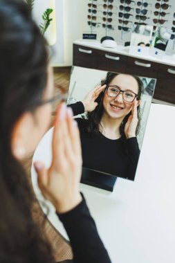 Optik dükkanı. Genç bir kadın bir optik mağazada gözlük seçer. Gözlüklü dur. Vizyon düzeltmesi. Gözlüklü kadın. Gözlüklü bir kadının portresi..