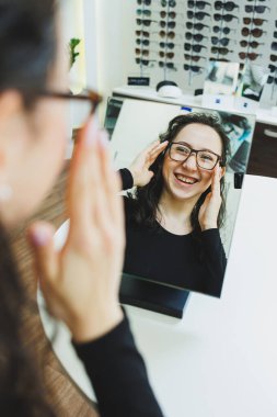 Optik dükkanı. Genç bir kadın bir optik mağazada gözlük seçer. Gözlüklü dur. Vizyon düzeltmesi. Gözlüklü kadın. Gözlüklü bir kadının portresi..