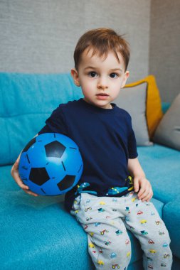 İki yaşında küçük bir çocuk elinde bir topla kanepede oturuyordu. Gelişmiş duygusal bir çocuk evde topla oynuyor.