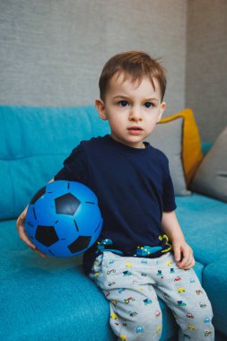 İki yaşında küçük bir çocuk elinde bir topla kanepede oturuyordu. Gelişmiş duygusal bir çocuk evde topla oynuyor.